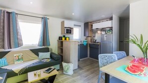 Un espace de vie compact comprenant un canapé, une table à manger, un coin cuisine avec un réfrigérateur et un four à micro-ondes, ainsi qu’une fenêtre avec des rideaux.