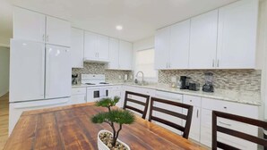 A modern kitchen with white cabinets, a wooden dining table, and a small potted plant. - Private Villa for Family and group getaway + pool (Murrells Inlet)
