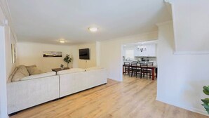 A modern living room with a sofa, a flat-screen TV mounted on the wall, and a dining area with a table and chairs. - Private Villa for Family and group getaway + pool (Murrells Inlet)