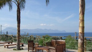 A terrace with wooden furniture, a rope barrier, and a view of the sea and mountains. - Residence Villaggio Petruso (Balestrate)