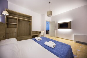 Ein Hotelzimmer mit einem Bett, einem Schrank, einem Schreibtisch, einem Stuhl, einem Fernseher und einer Tür zu einem anderen Raum.