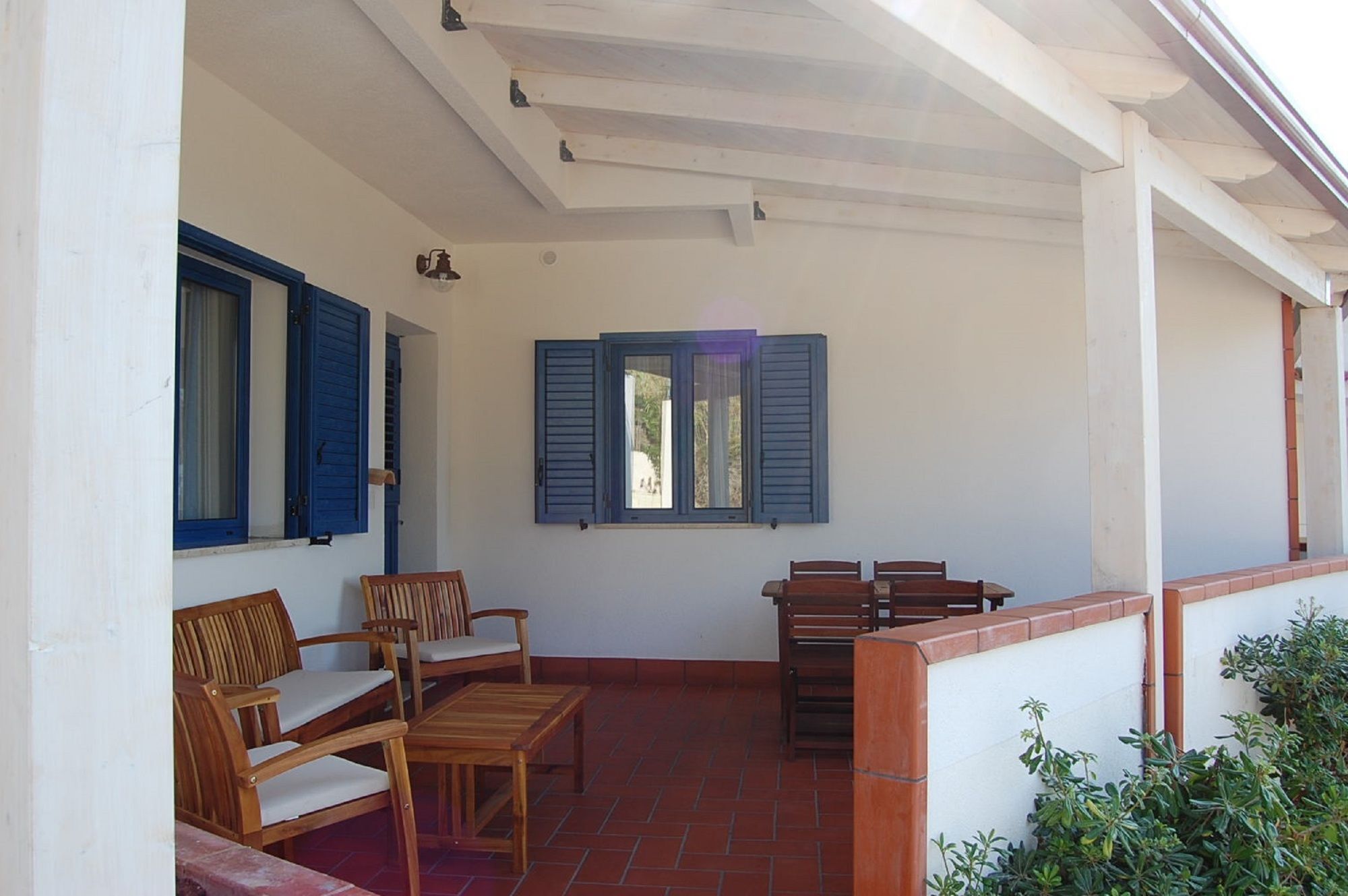 A covered outdoor seating area with wooden furniture and a tiled floor.