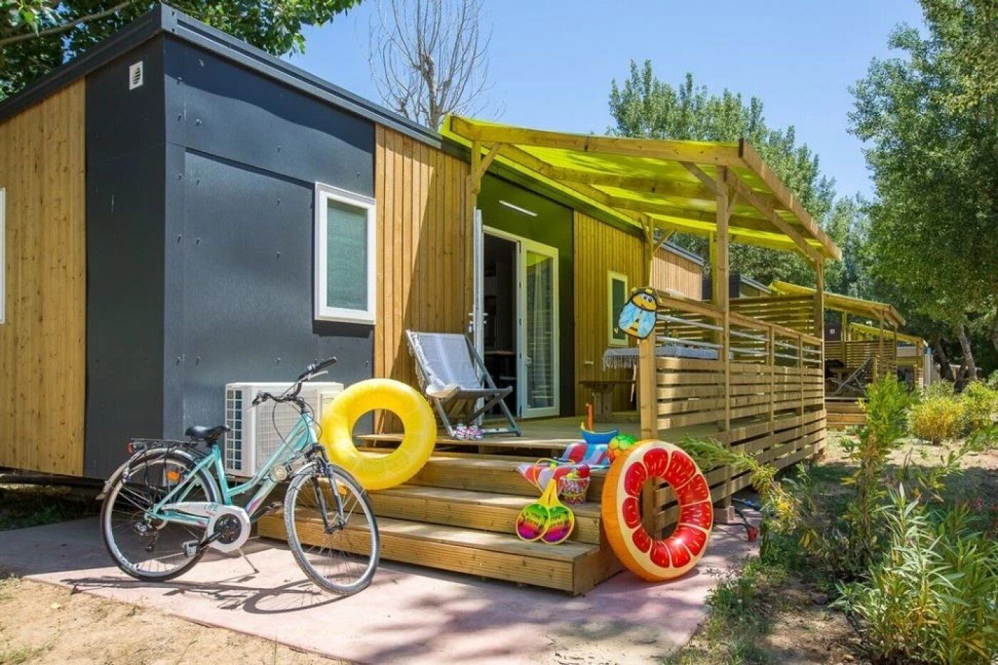A small cabin with a wooden deck, a bicycle, and inflatable pool toys.