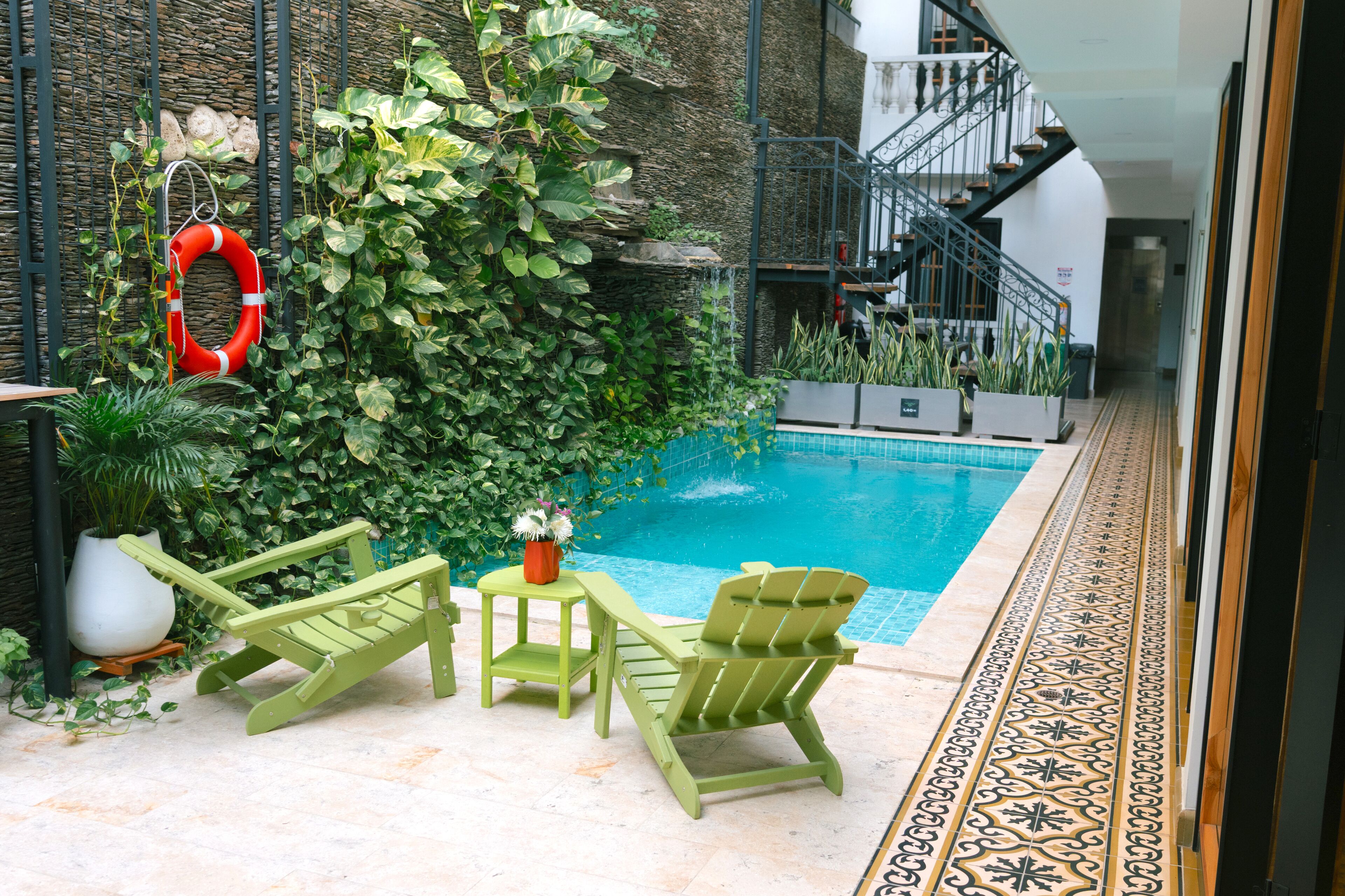 Un espace piscine équipé d’une bouée de sauvetage, de chaises vertes et d’une plante en pot.