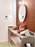 Un baño con tocador de madera, lavabo de cobre y un espejo grande.