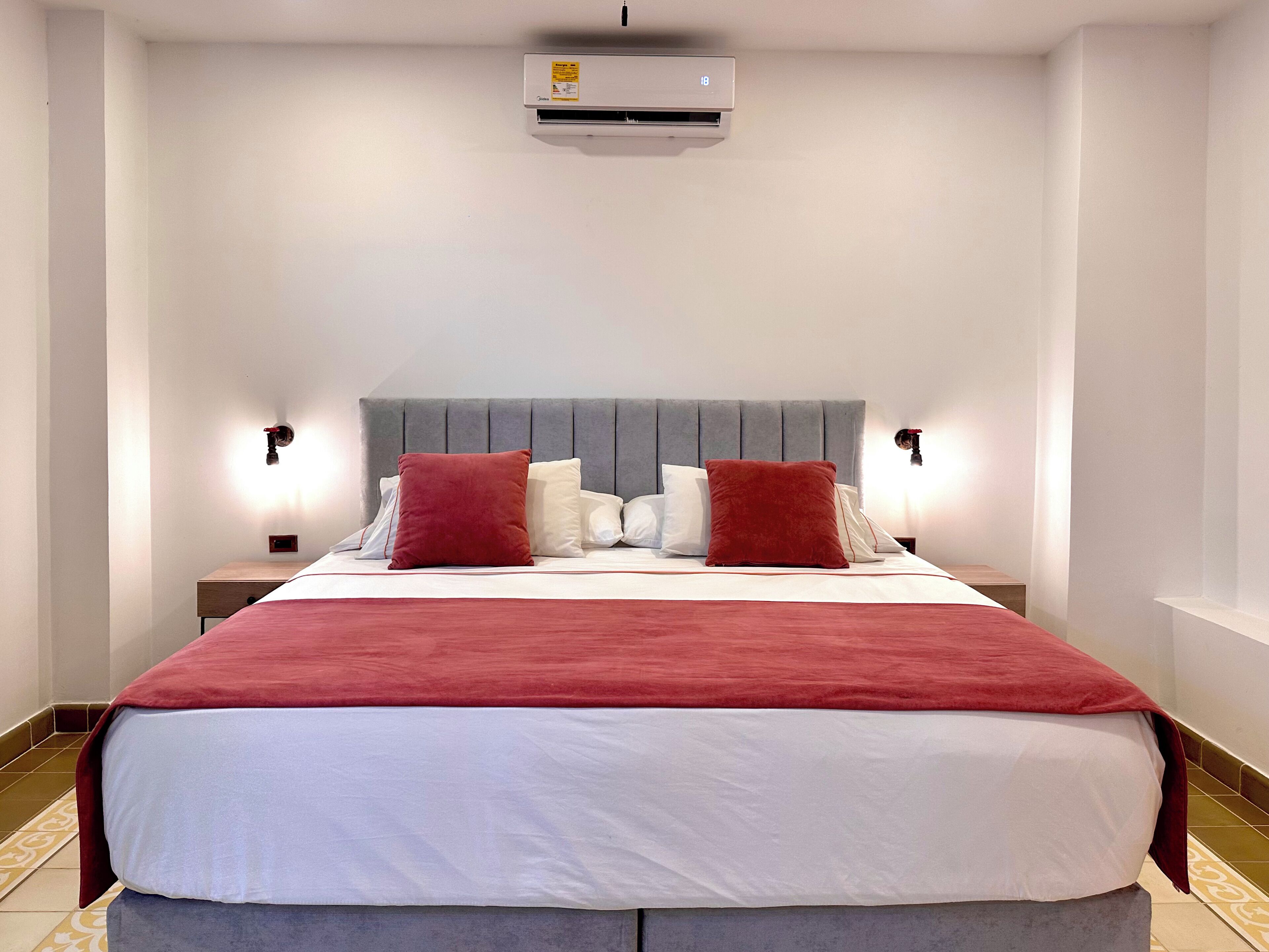 Une chambre d’hôtel équipée d’un lit, d’une table de chevet, d’un climatiseur et de deux lampes fixées au mur.
