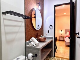 A modern bathroom with a large mirror, a towel rack, a sink with a copper basin, and a toilet.