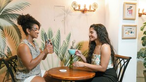 Two people seated at a round wooden table with a small vase and a cup on it. - La Brisa Loca Prime (Santa Marta)