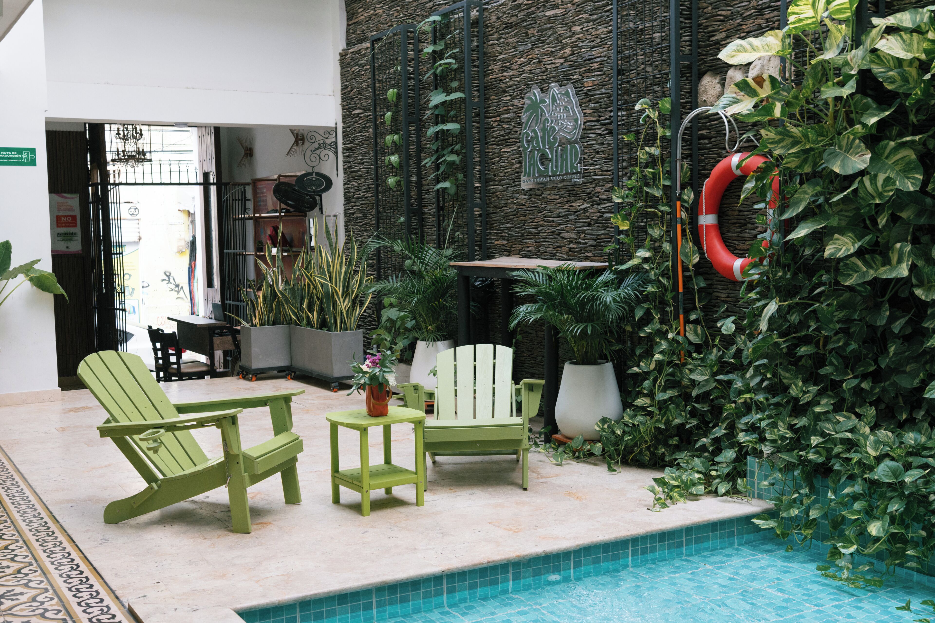 A pool area with a lifebuoy, green Adirondack chairs, and potted plants.