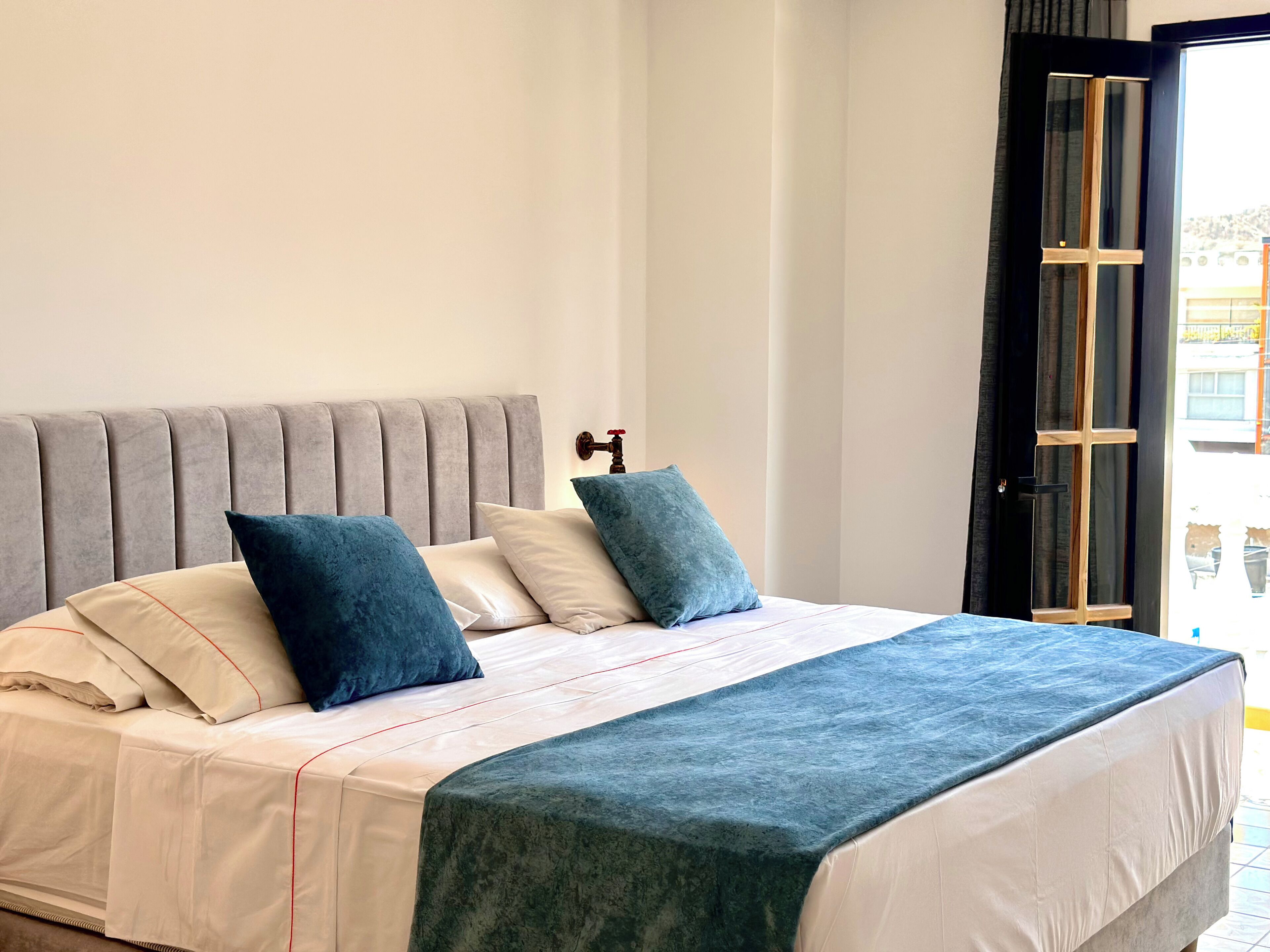 Ein Bett mit grauem Polsterkopfteil, weißen Leinen und Kissen in Türkis und Weiß.