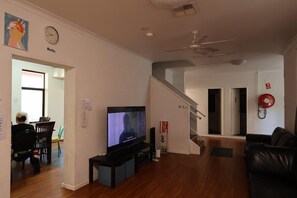 A living room with a flat-screen TV, wooden flooring, a ceiling fan, and a staircase leading to another level. - Downtown Backpackers Hostel (Perth)