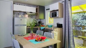 A compact kitchen with a dining area, a microwave, and a window with a view of greenery. - ZEcamping 4* parc aquatique animations locatif TV LV clim 4 pers (Sérignan)
