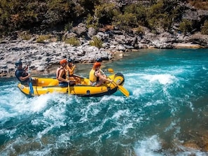 A group of people in a yellow raft on a river surrounded by rocky terrain.