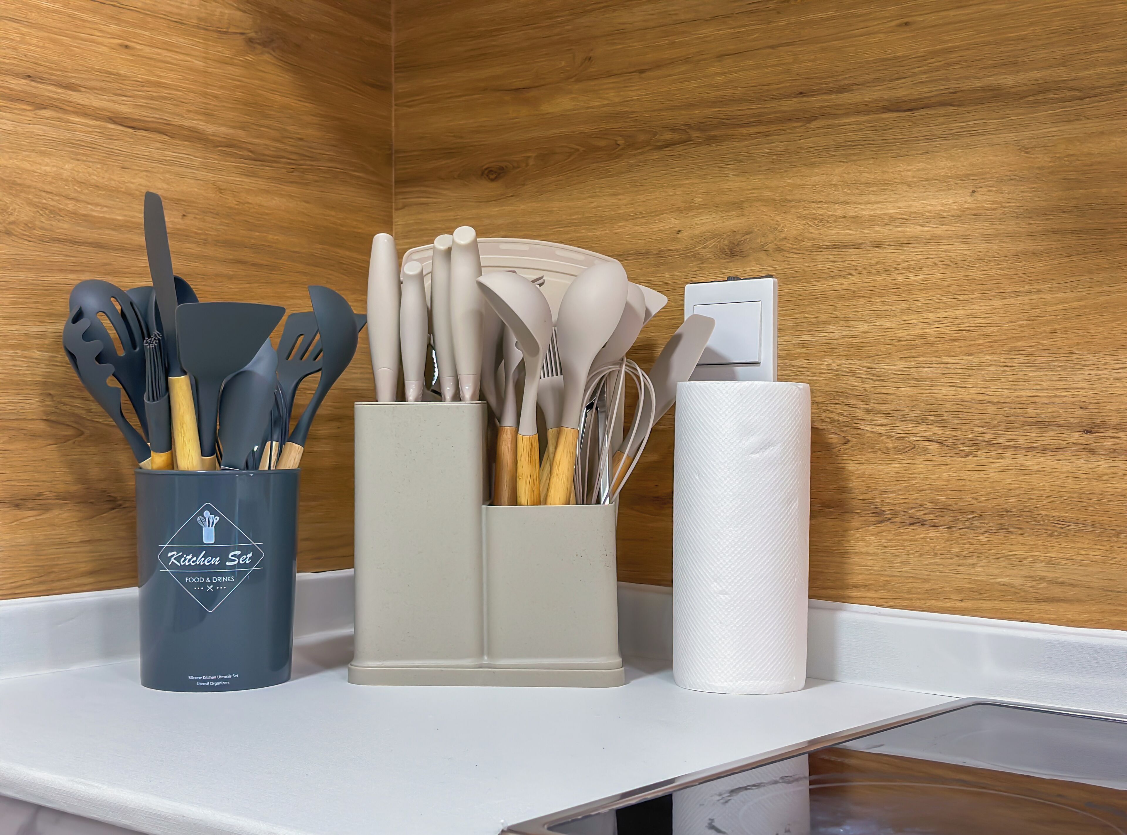 A kitchen counter with a utensil holder, a paper towel dispenser, and a power outlet.