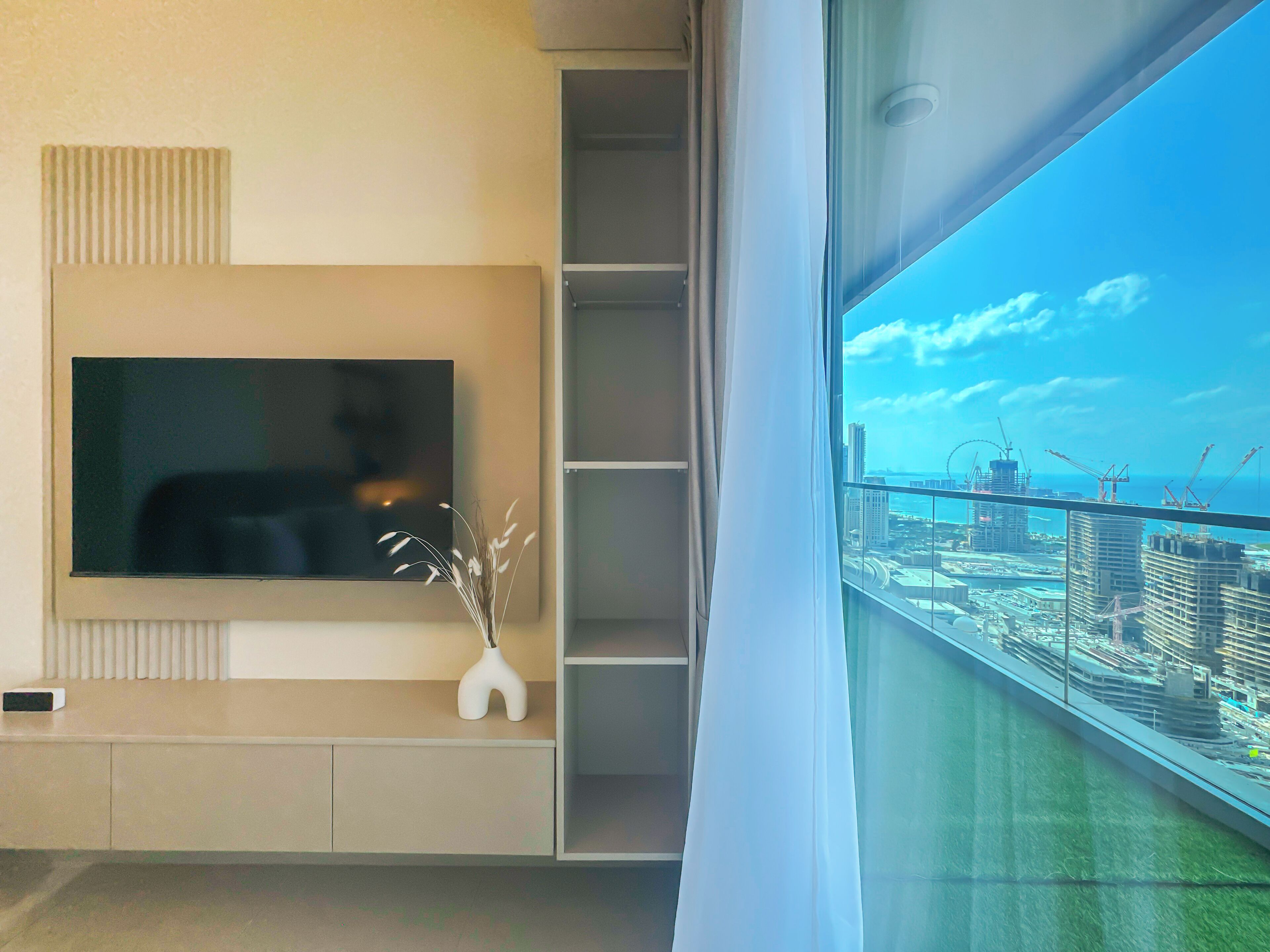 A modern living room with a large TV, a decorative vase, and a view of a cityscape through a balcony.