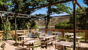 Un patio al aire libre con mesas y sillas, una terraza de madera y vistas a un lago y colinas.