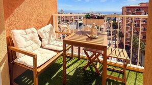Un balcón con mesa y sillas de madera, un sofá acolchado y vistas a la ciudad.
