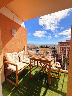 A balcony with a wooden table and chairs, a cushioned sofa, and a view of the cityscape. - BONANZA 1 SUNNY BEDROOM APARTMENT, NEW 2026! (Arroyo de la Miel)