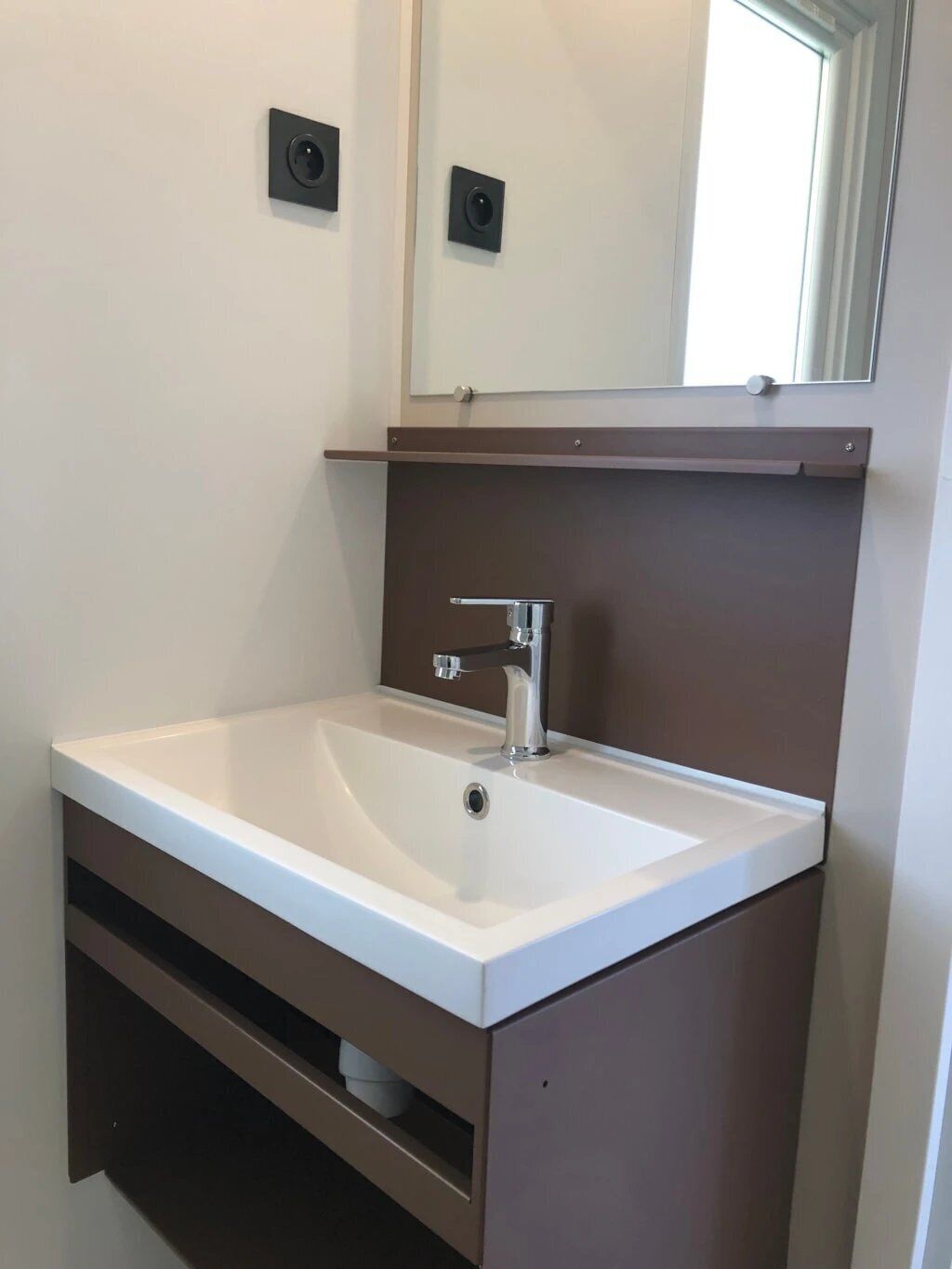 A bathroom with a white sink, a mirror above it, and a brown cabinet below.