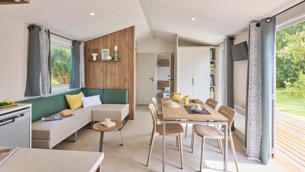 Een moderne woonkamer met een bank, salontafel en een eetgedeelte met stoelen. Er is een houten accentmuur met een 'TEA' bord.