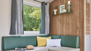 Een moderne woonkamer met een groene bank, een ronde houten salontafel en een raam met gordijnen.