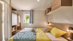 Een slaapkamer met een bed, een raam met gordijnen, een kledingkast en een nachtkastje met een lamp.