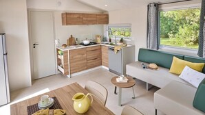 Een compacte leefruimte met een kitchenette, een eethoek en een zithoek met uitzicht op groen.