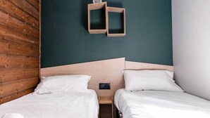 Camera con due letti, una testiera in legno, parete verde scuro e un piccolo ripiano con un oggetto rotondo.