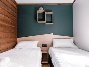 Ein Zimmer mit zwei Betten, einem Holz-Kopfteil, einer dunkelgrünen Wand und einem kleinen Holzregal mit einem runden Gegenstand.
