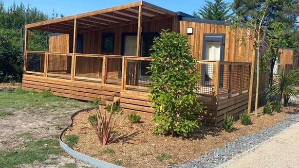 Una baita di legno con un portico coperto, un piccolo giardino e cielo sereno.