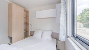 Un dormitorio con cama, armario, ventana con vistas y cortina.