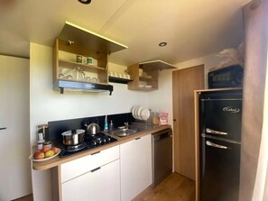 Eine kleine Küche mit einem schwarzen Kühlschrank, einem Herd und einem Spülbecken. Es gibt Schränke und eine Arbeitsplatte mit verschiedenen Gegenständen darauf.