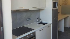 A modern kitchen with white cabinets, a black stove, and a microwave. - Santo George Beach (Malevizi)