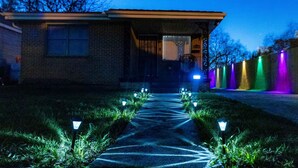 Une maison avec un chemin menant à la porte d’entrée, entourée de pelouse et de petits arbres.