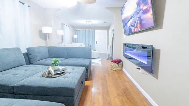 Un salon moderne avec un canapé d’angle, un téléviseur à écran plat fixé au mur et un plancher en bois.