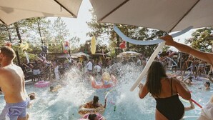 Área de piscina com brinquedos infláveis e pessoas aproveitando a água.