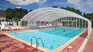 Una piscina con cerramiento de vidrio, rodeada de sillas de descanso y una zona techada.