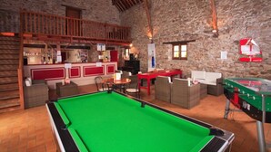 Una sala de billar con mesa de pool, zona de estar y mesa de fútbolín.