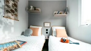 A bedroom with two beds, each with a pillow and a small shelf above. - ZEcamping 3* animaux acceptés locatif TV clim 23m2 4 pers (Divonne les Bains)