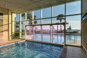 An indoor swimming pool with clear glass walls, a tiled floor, and a view of palm trees and a distant building. - Aqua Sunset Retreat | Beachfront Condo w/ Large Balcony | Aqua 2003 (Panama City Beach)