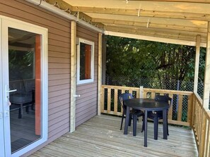 Eine überdachte Terrasse mit Tisch und Stühlen, eine Glasschiebetür und ein Holzgeländer.