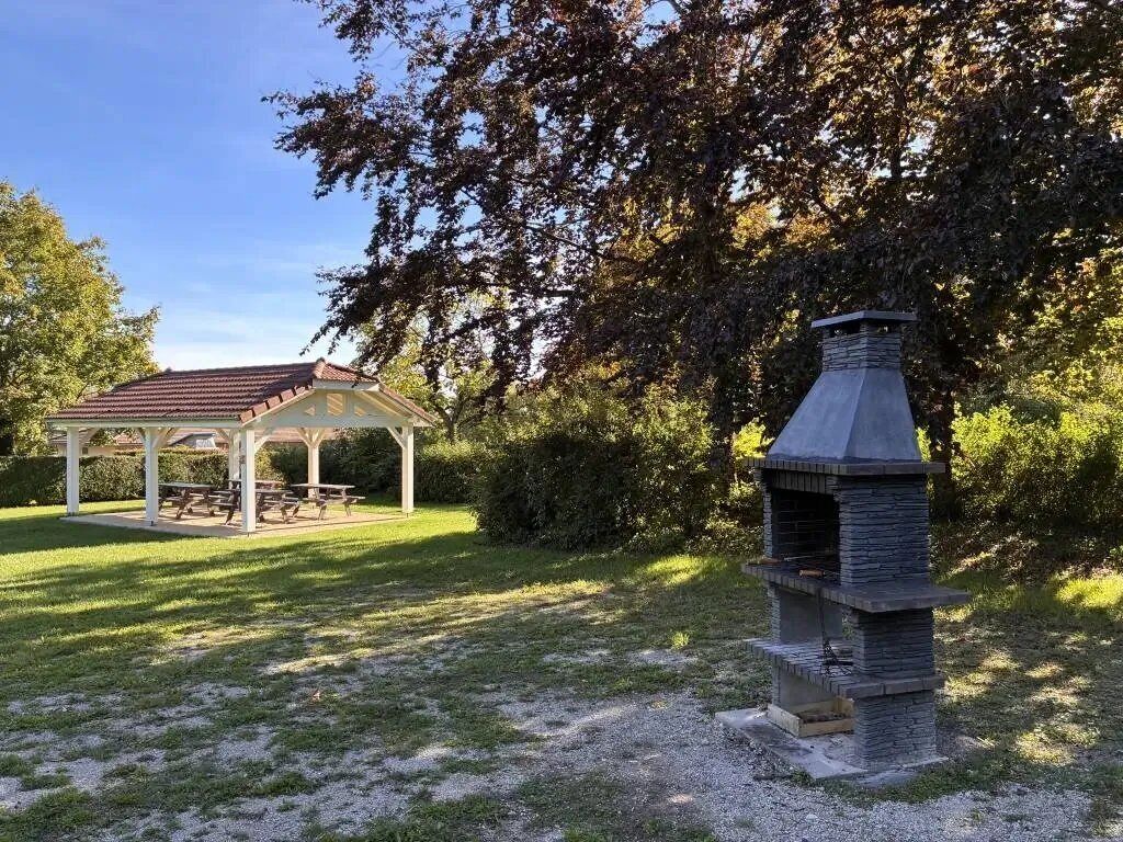 A gazebo with picnic tables, a stone barbecue grill, and a grassy area.