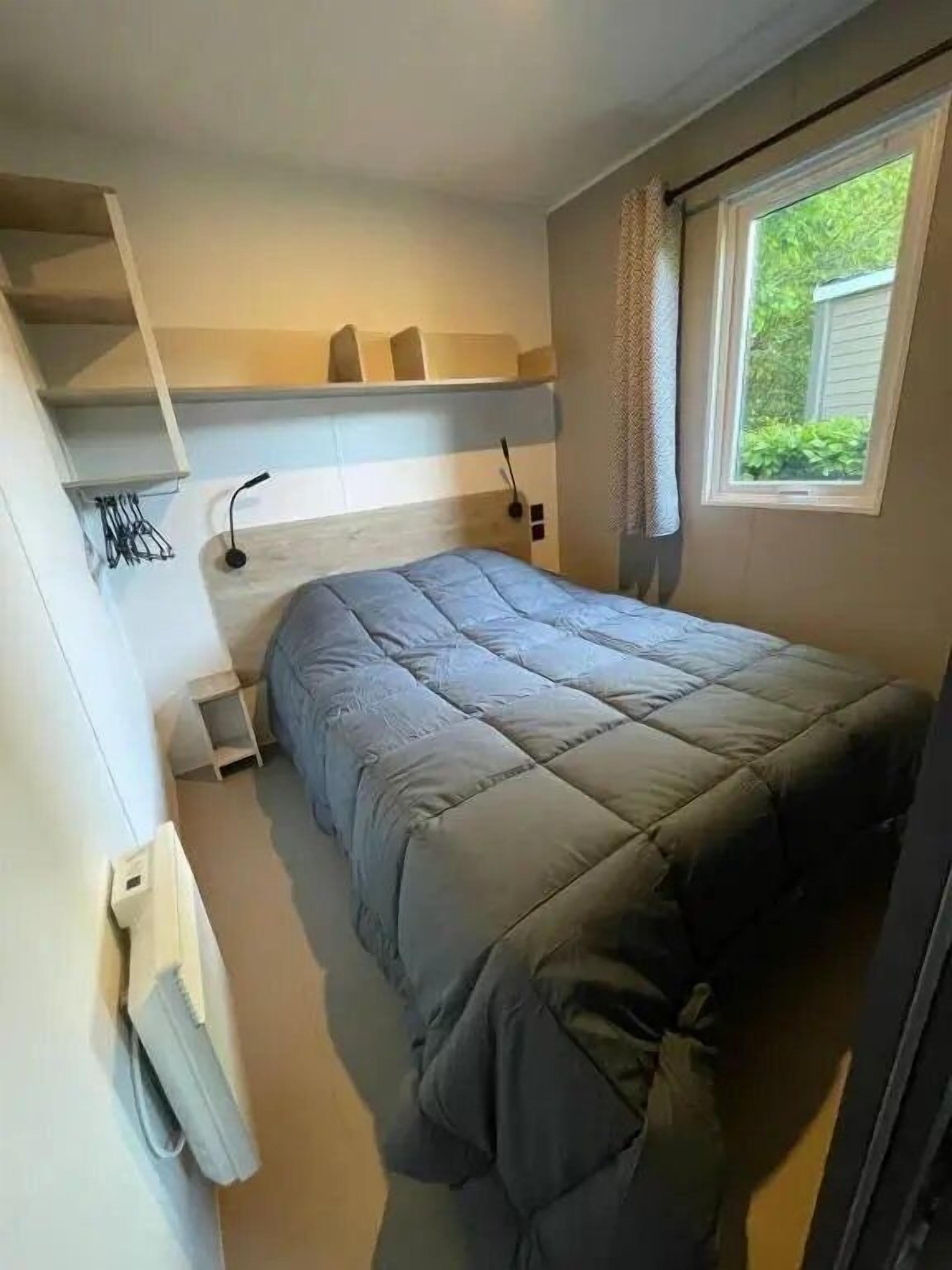 Et soveværelse med en seng, et vindue, en hylde med genstande og en radiator.