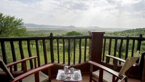 Ein Balkon mit einem für Tee gedeckten Tisch, mit Blick auf eine Savannenlandschaft und entfernte Berge.