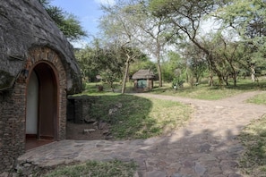 Un sentier de pierres mène à un bâtiment rustique doté d’un toit de chaume et d’une entrée en arc de cercle.