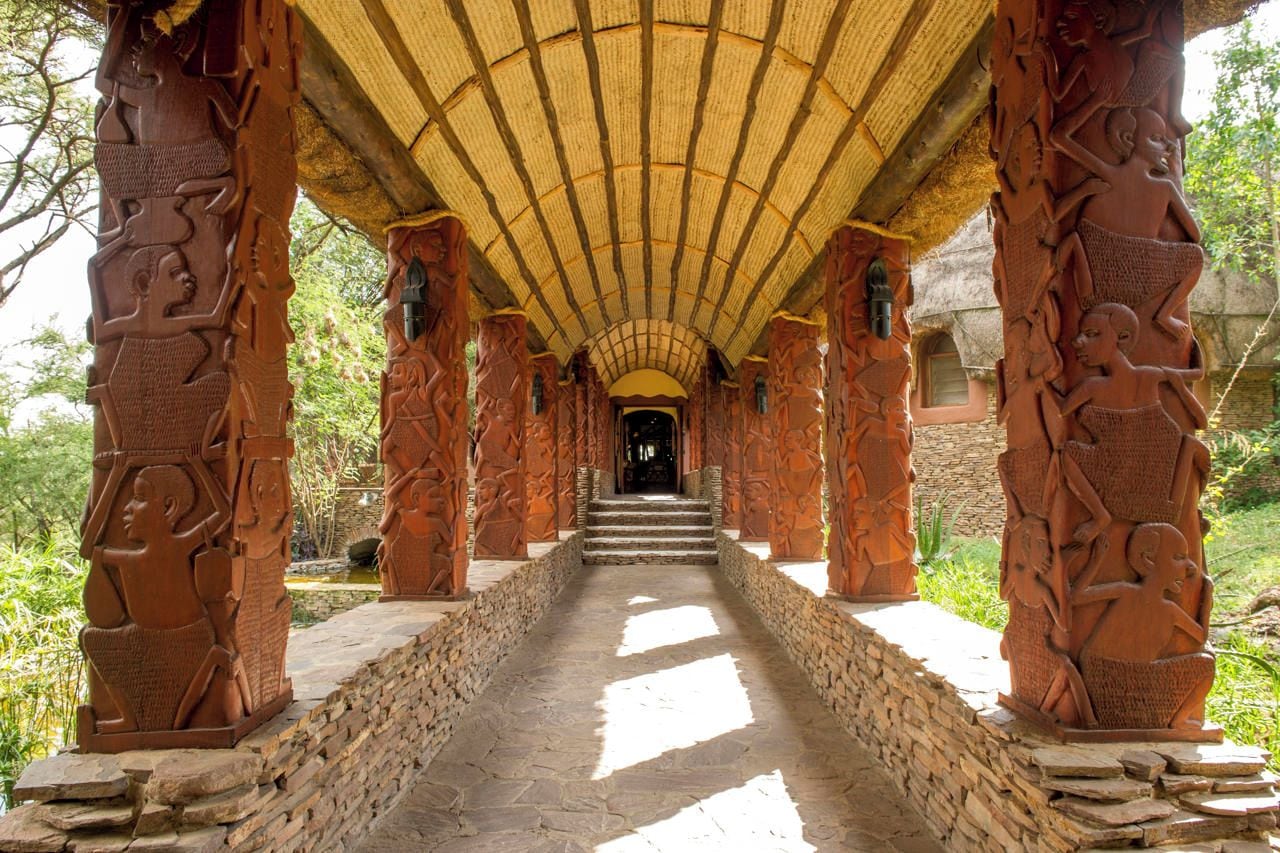 Un pasillo con escalones de piedra que conducen a una puerta, flanqueado por columnas ricamente talladas.