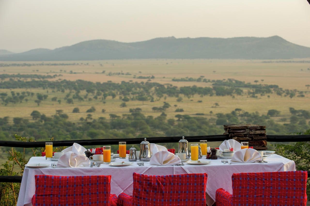 Una mesa de comedor para dos personas con vista a un paisaje de sabana.