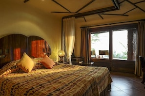 A bedroom with a large bed, a nightstand, a lamp, and a view of the outdoors through a window. - Serengeti Serena Safari Lodge (Serengeti)
