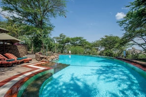 Una piscina con pared de piedra y sillas de descanso.