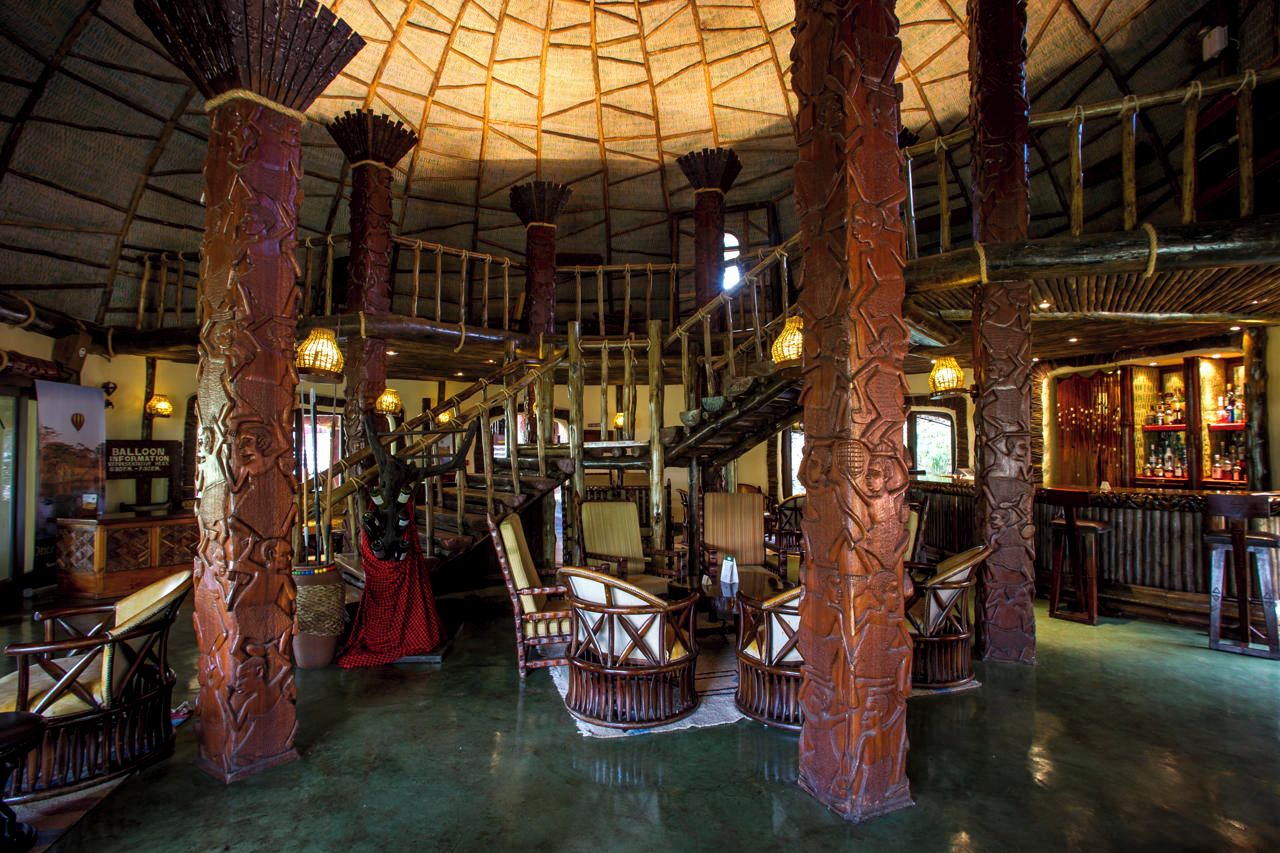 A spacious interior with high wooden pillars, a bar area, and a staircase leading to an upper level.